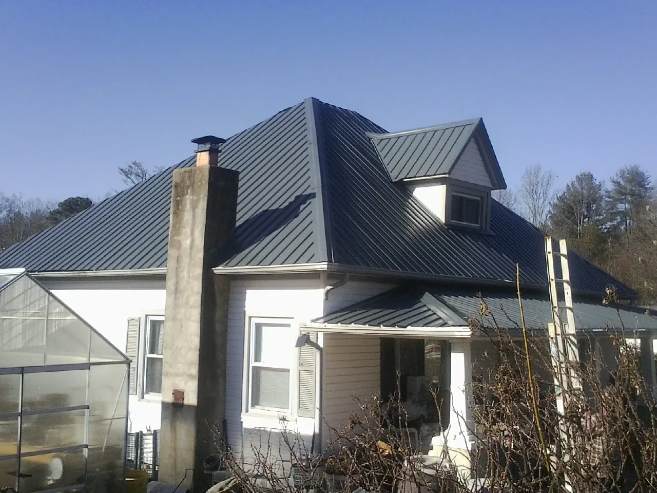 Dark blue standing seam metal roof on a white farmhouse with dormer — Slate & Tile Roof Repair by Roofing Brothers in Exline