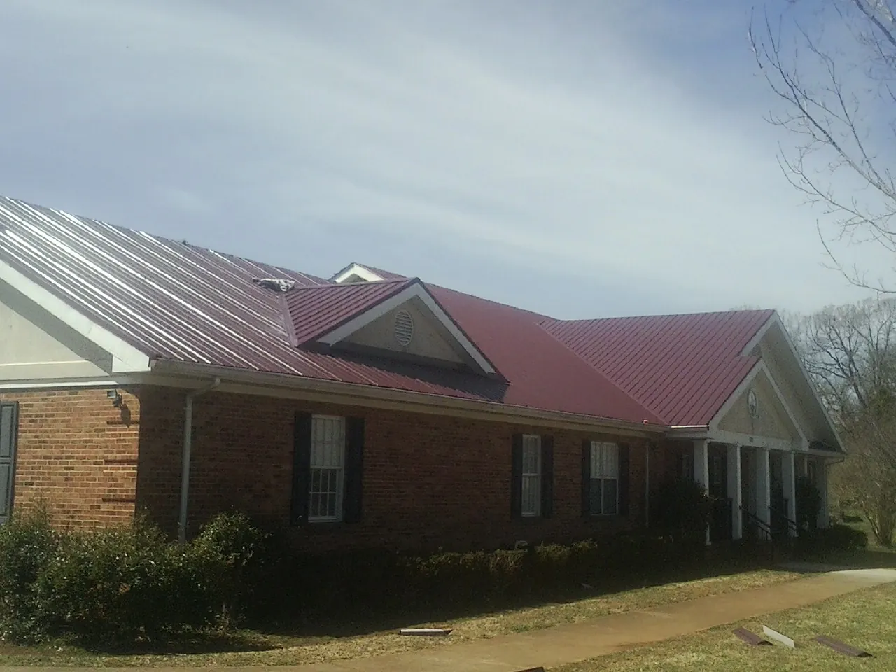 Red metal roof with gabled entries on a long brick building, from a Hail Damage Roof Repair job in Exline