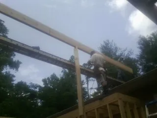 Carpenter setting a ridge beam over a new addition frame in Exline