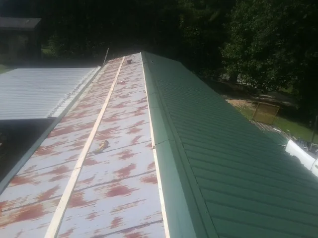 Old rusted panels beside newly installed green metal roofing — Wind Damage Roof Repair by Roofing Brothers in Exline