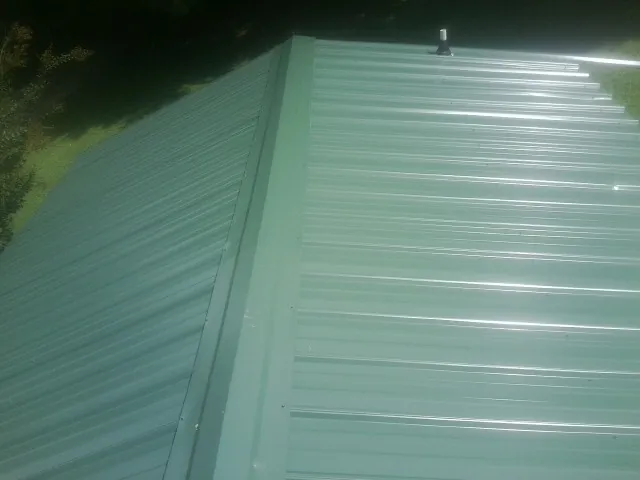 New green metal panels meeting at the ridge of a roof — Flat Roof Repair work by our crew in Exline