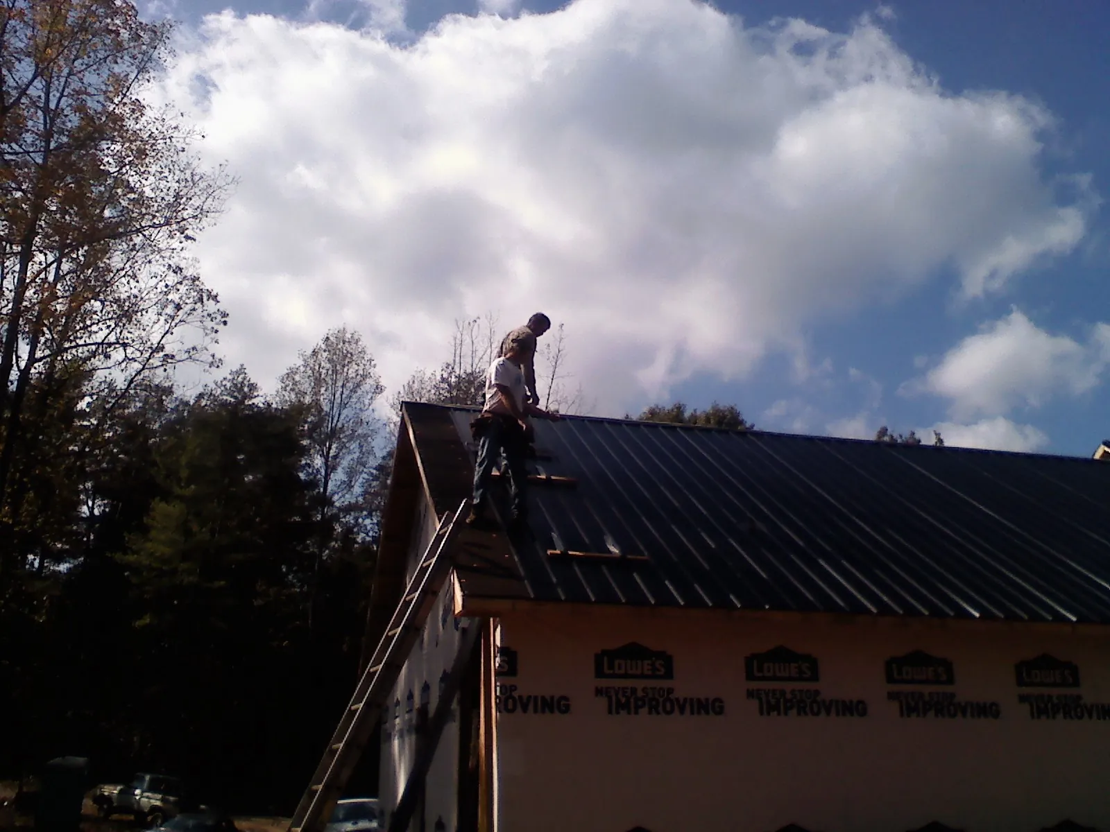 Roofer fastening dark metal panels high against a cloudy sky, from a Roof Inspection job in Exline