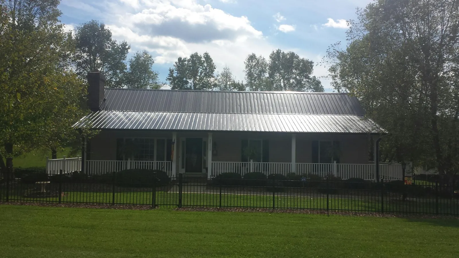 Gray metal roof on a brick ranch with a full width front porch — Gutter Guard Installation work by our crew in Exline