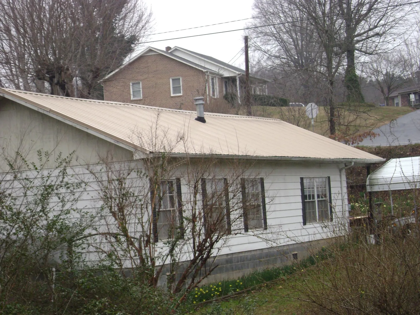 Tan metal roof on a white sided house set into a hillside — Commercial Roofing by Roofing Brothers in Exline
