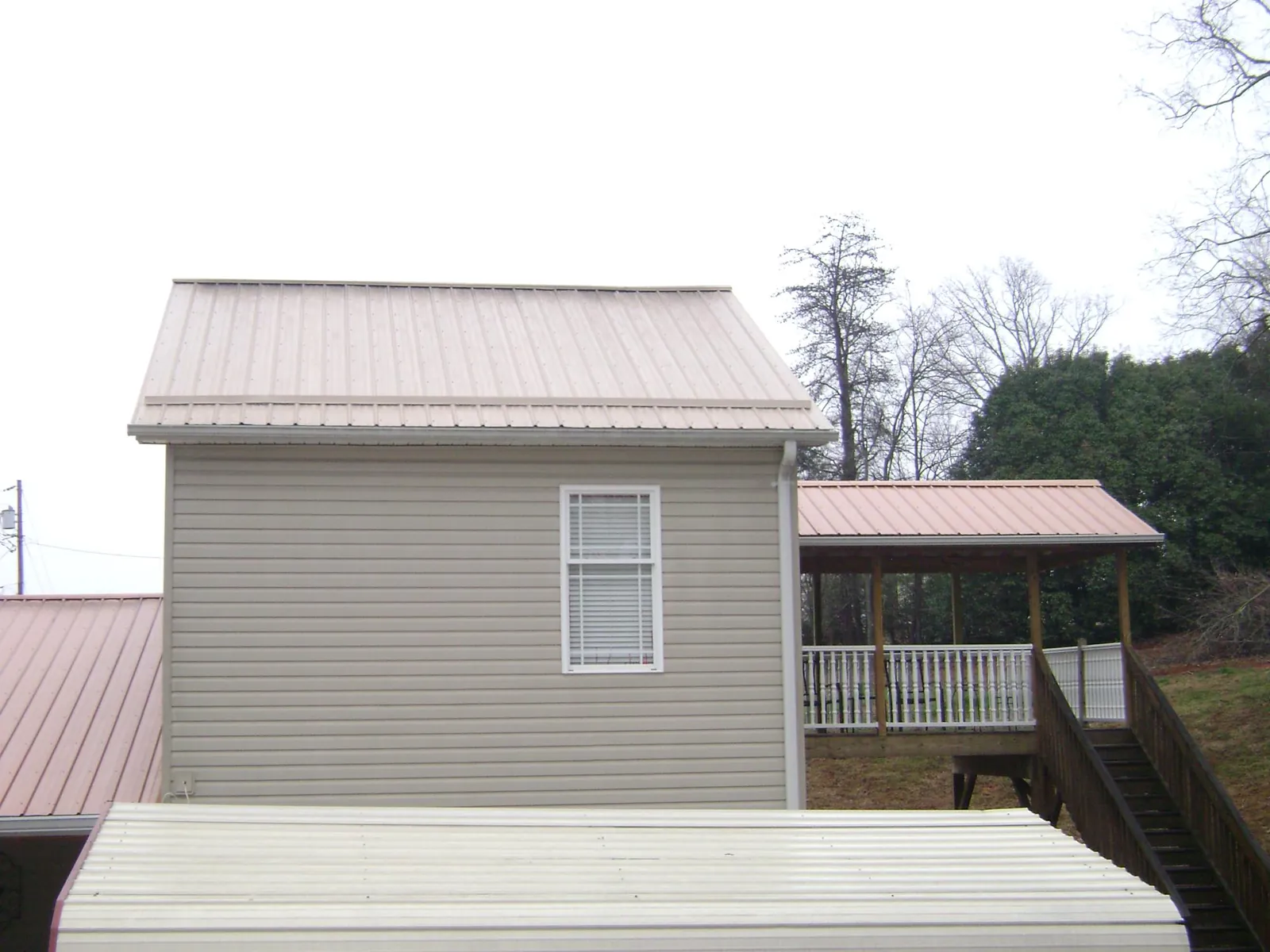 Tan metal roofs on a two story addition and attached porch, from a Roof Replacement job in Exline